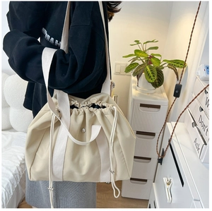 Close-up of beige drawstring tote bag with silver metal buckle and wide fabric shoulder strap
