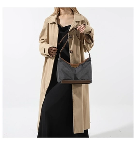 Detail view of charcoal nylon moon bag with brown leather strap worn on khaki trench coat