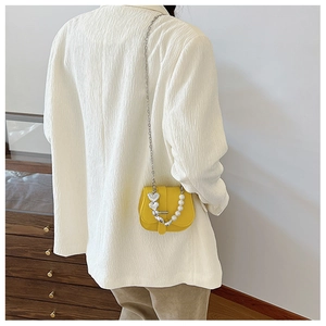 Détail du mini sac jaune avec chaîne en perles et breloque cœur sur un blazer blanc