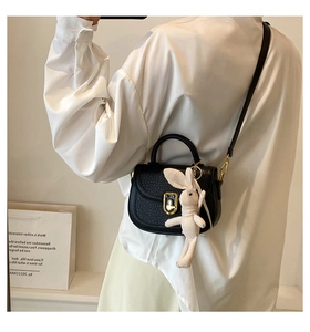Detail of black textured crossbody bag with gold buckle and cute rabbit doll charm