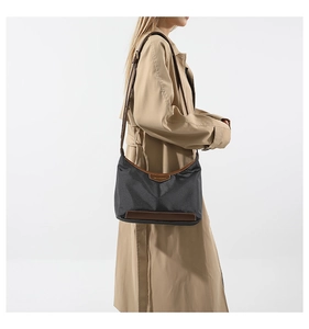 Minimalist nylon crossbody bag in black with brown leather trim worn by model in trench coat