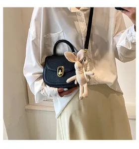 Detail of black pebbled leather saddle bag with gold lock and a beige bunny charm