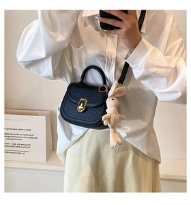 Detail of black pebbled leather crossbody bag with gold heart lock and cute rabbit charm