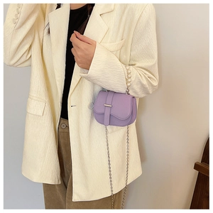 Détail du sac selle violet avec poignée en perles et chaîne argentée sur blazer beige