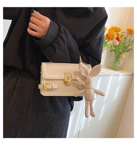 Détail d'un sac à bandoulière en cuir blanc avec boucle dorée et breloque lapin