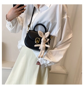 Close-up of black litchi grain leather saddle bag with gold buckle and cute rabbit charm