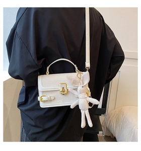 Détail du sac bandoulière blanc à motif litchi avec boucle dorée et pendentif lapin