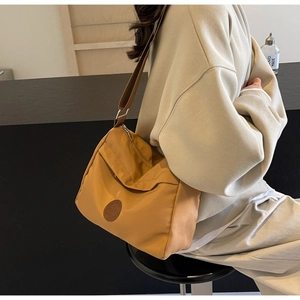 Detail of a ginger yellow nylon crossbody bag with circular leather logo and wide strap