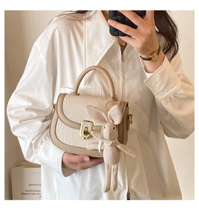 Detail of beige saddle bag with gold metal twist lock and cute knitted rabbit charm