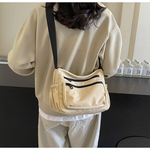 Detail of minimalist beige nylon crossbody bag featuring multi-pocket zippers and drawstring