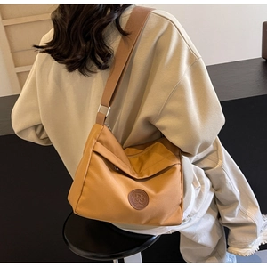 Detail of caramel nylon crossbody bag featuring wide strap and circular logo on smooth fabric