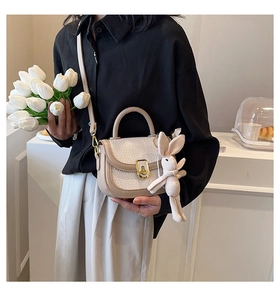 Detail of cream white faux leather bag with gold lock and cute bunny charm on handle