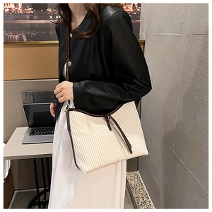 Fashionable cream tote bag with vertical texture and brown straps shown on a model
