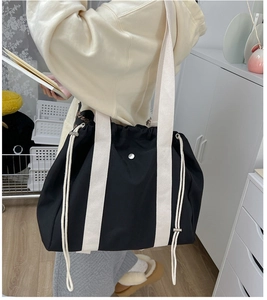 Detail of large black canvas tote bag showing drawstring closure and wide shoulder strap