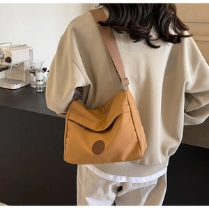 Side view of woman wearing a large ginger canvas crossbody bag in a modern cafe setting