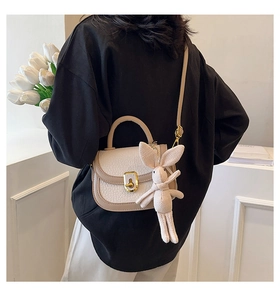 Close-up of beige textured leather crossbody bag with gold lock and rabbit pendant