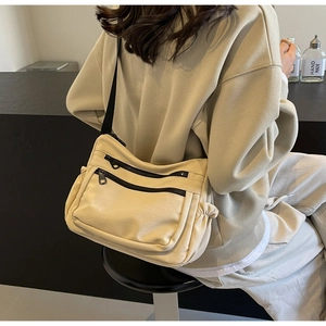 Detail view of a beige canvas crossbody bag with black zippers on a model back