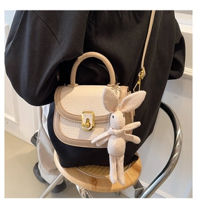 Detailed side view of a beige PU leather crossbody bag featuring a cute bunny charm and gold lock