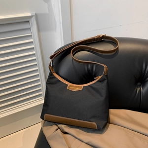 Minimalist black nylon handbag with brown leather trim displayed on a leather sofa