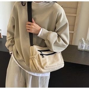 Detail of beige nylon crossbody bag with multi-pocket design and wide black shoulder strap