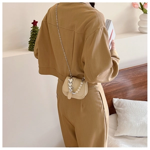 Détail d'un sac bandoulière beige demi-lune avec charms cœurs et chaîne de perles