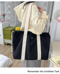 Detail of black canvas tote bag with drawstring closure and wide beige shoulder strap