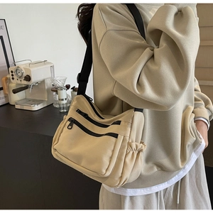 Detail of beige canvas crossbody bag featuring functional black zippers and utility style