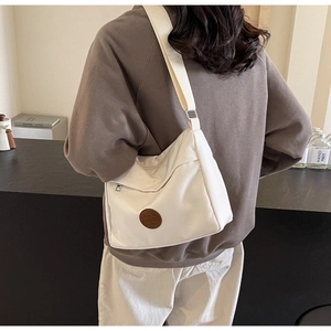 Detail of white canvas crossbody bag featuring brown circular logo and wide woven strap