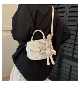 Detail of cream white pebbled leather bag with golden clasp and cute knitted bunny charm
