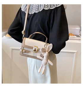 Gros plan du sac bandoulière crème avec texture litchi et charmant lapin en tricot attaché