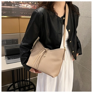 Detail of beige pleated shoulder bag with decorative drawstring on a model in minimalist setting