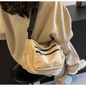 Detailed back view of a beige canvas crossbody bag with multiple pockets and adjustable strap