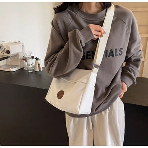 Detailed view of white canvas crossbody bag with brown leather logo and wide fabric strap