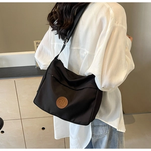 Detail of a black nylon messenger bag with a brown logo patch and wide shoulder strap