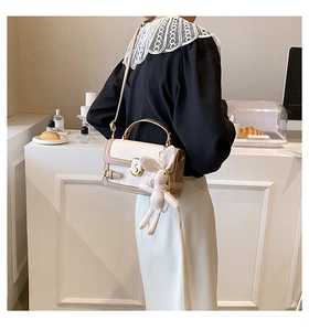 Détail d'un sac bandoulière beige et marron avec boucle dorée et breloque lapin