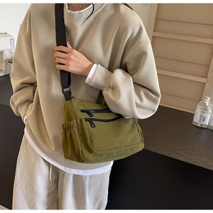 Detail of army green canvas crossbody bag featuring multi-pocket design and brown strap