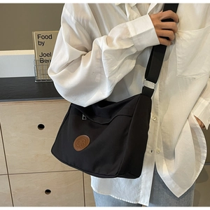 Detail of black canvas messenger bag with round brown leather logo and wide strap