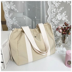 Minimalist beige drawstring tote bag with wide white shoulder strap in canvas material