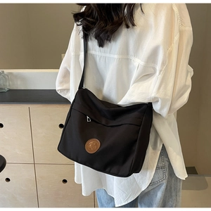 Detail shot of a black nylon crossbody bag with leather logo patch worn by a model