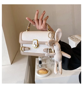 Détail d'un sac à main beige grainé avec fermoir doré et pendentif lapin décoratif