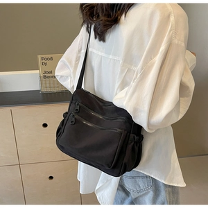 Detailed view of black multi-pocket nylon crossbody bag with adjustable wide strap on model