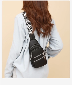 Detail of black pebbled leather crossbody bag with three zippers and geometric strap