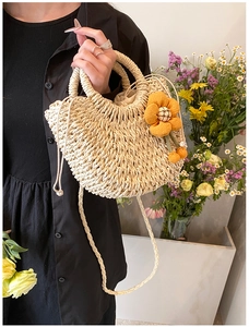 Detail view of straw shoulder bag with woven texture and orange flower accessory