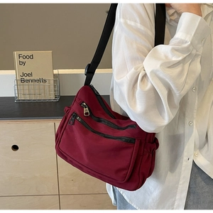 Detail of burgundy waterproof nylon crossbody bag with multiple zippers shown on a model