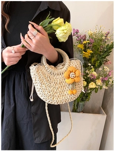 Detail of hand-woven beige straw bag with a 3D orange floral charm and drawstring closure