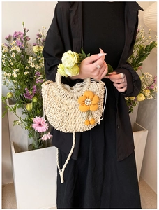 Detail of a half-round straw bag with orange floral charm and natural weave texture