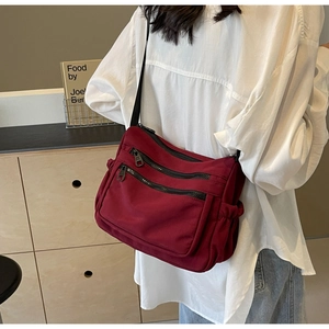 Detail of burgundy nylon crossbody bag with three zippers shown on a model