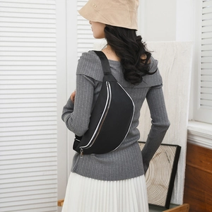 Detail of a black crescent chest bag with white trim worn by a model in a bright interior