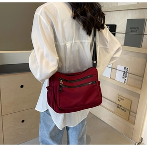Detail of burgundy nylon crossbody bag featuring multiple zipper pockets and side pockets