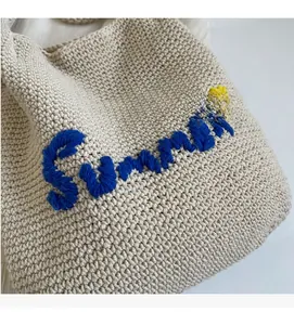 Gros plan du sac à main tissé beige avec broderie Summer bleue et détail d'étoile jaune vif
